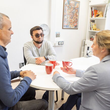 Drei Menschen sitzen in einem Büro um einen runden Tisch ins Gespräch vertieft.