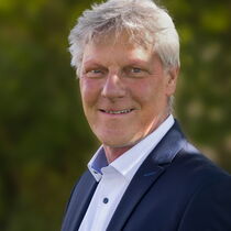 Portraitfoto Maarten Kubeja - er hat kurzes graues Haar und trägt ein blaues Sakko über einem weißen Hemd.