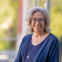 Portraitfoto Barbara Krönert-Ritz - sie hat kinnlanges gewelltes Haar, trägt eine Brille und ein blaues Oberteil.