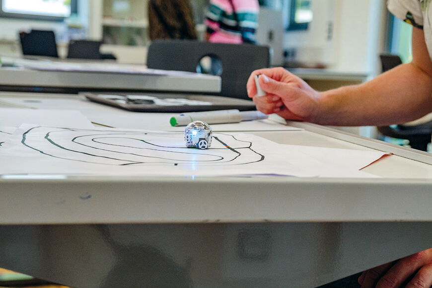Auf einem Tisch fährt ein kleiner Ozobot über eine auf Papier gezeichnete Linie.