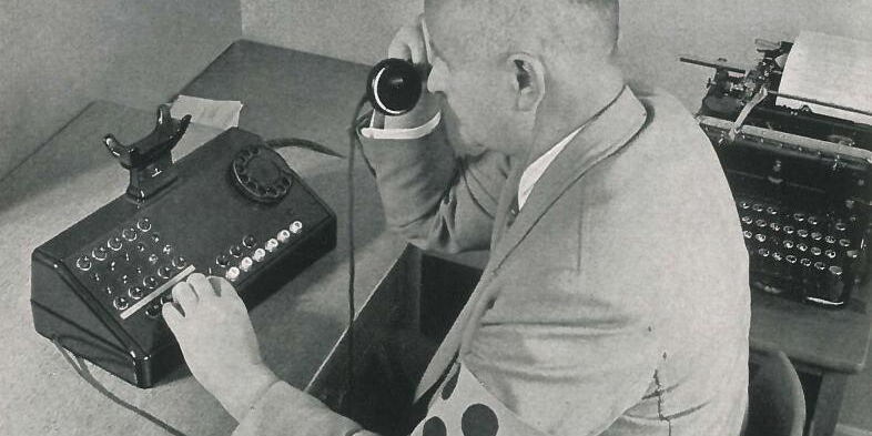 Historische Schwarzweißfotografie: Ein Mann mit Blinden-Armbinde sitzt an einem Vermittlungspult.