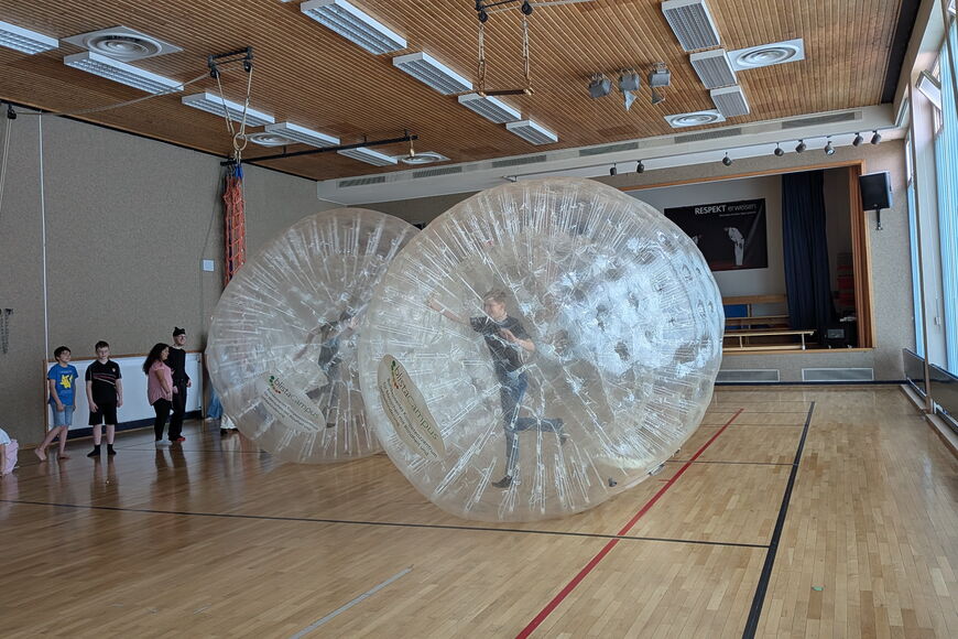 In der Gymnastikhalle laufen Kinder in durchsichtigen Zorbingbällen umher.