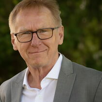 Portraitfoto Werner Hecker - er trägt kurzes Haar, eine Brille und ein graues Sakko über einem weißen Hemd.