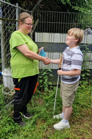 Übergabe der Spende im Außenbereich des Tierheims: Noel schüttelt einer Mitarbeiterin des Tierheims die Hand, sie hält einen Umschlag in der anderen Hand.