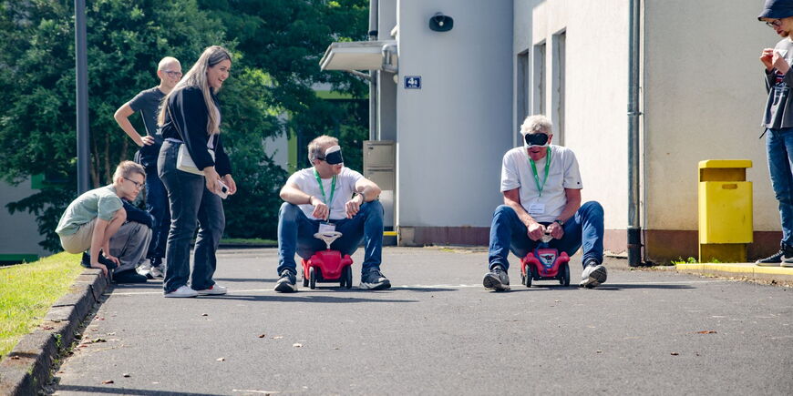 Unter den Augen der Besucher sitzen Patrick Temmesfeld und Maarten Kubeja mit verbundenen Augen auf Bobbycars.
