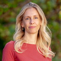 Portraitfoto Susanne Deertz - Sie trägt das hellblonde offen und hat ein korallenrotes Kleid an.