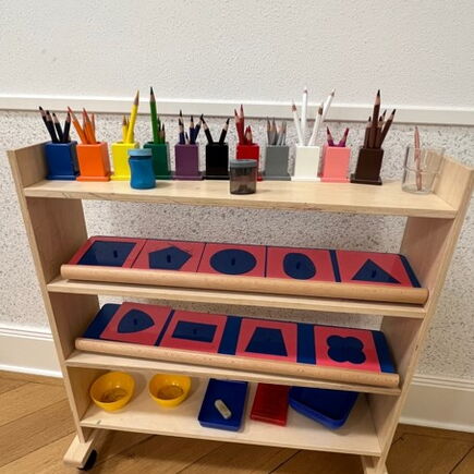Auf einem Holzregal stehen bunte Stifte und geometrische Formen.