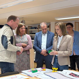 Astrid Wallmann bei ihrem Besuch in der blista: sie hat 3D Gedruckte Modelle in der Hand, mehrere Personen scheinen im Gespräch mit ihr.
