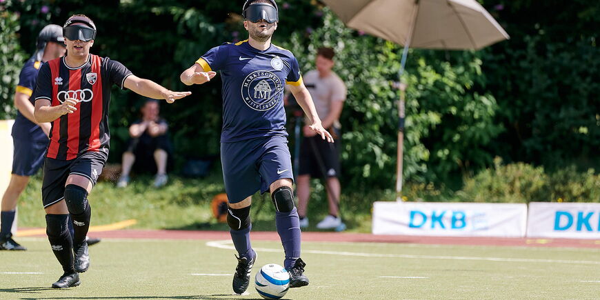 Ein Blindenfußballspieler dribbelt eine Ball, ein Gegner ist ihm auf den Fersen.