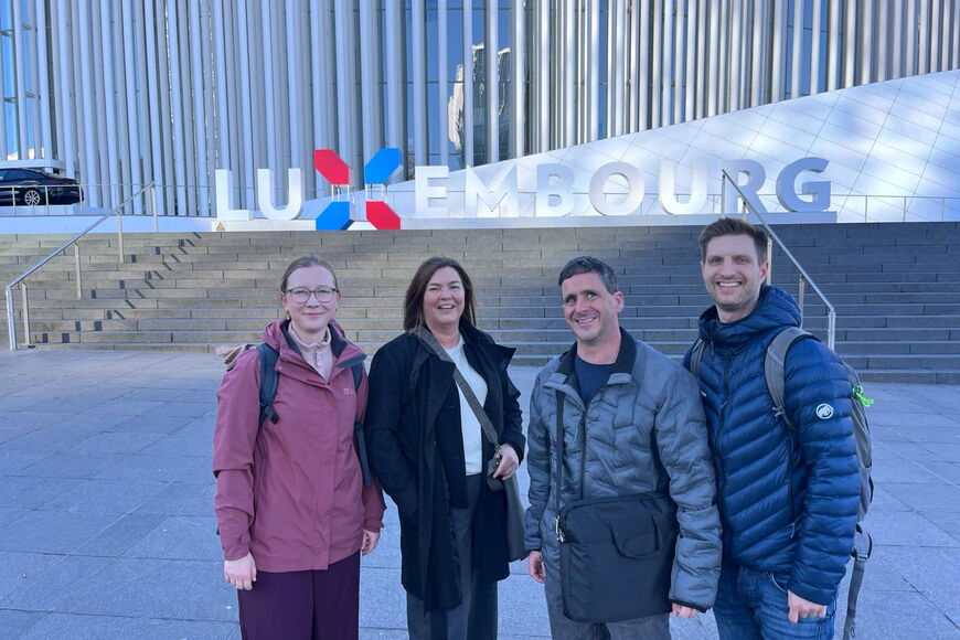 Debora Debes, Silke Roesler, Jens Flach und Michael Völcker stehen in winterlicher Kleidung auf einem Platz vor einer Treppe, über der der Schriftzug „Luxembourg“ prangt.