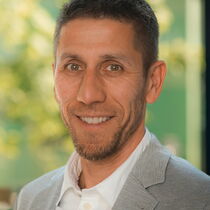 Portraitfoto Daniel Reh - er lächelt freundlich in die Kamera, hat kurze braune Haare und einen drei-Tage-Bart.