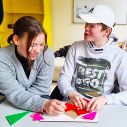Eine Schülerin und ein Schüler sitzen in einem Klassenraum und puzzeln mit dreieckigen Teilen eines MuLi-Lernpaketes.