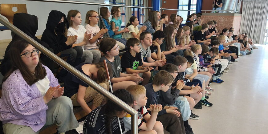Auf den Sitzbänken der Aula reihen sich zahlreiche Schüler*innen von CSS und MSM in Erwartung des Känguru-Wettbewerbs.