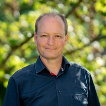 Portraitfoto Tobias Mahnke - Er trägt kurzes Haar und ein dunkelblaues Hemd.