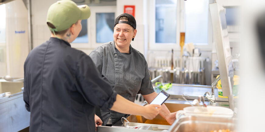 Zwei Köchinnen stehen in einer Großküche und bereiten Essen zu.