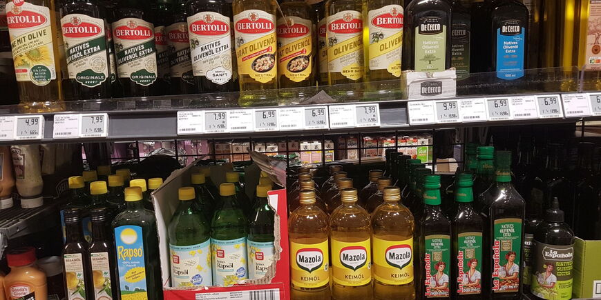 In einem supermarktregal stehen verschiedene Flaschen Raps- und Olivenöl.