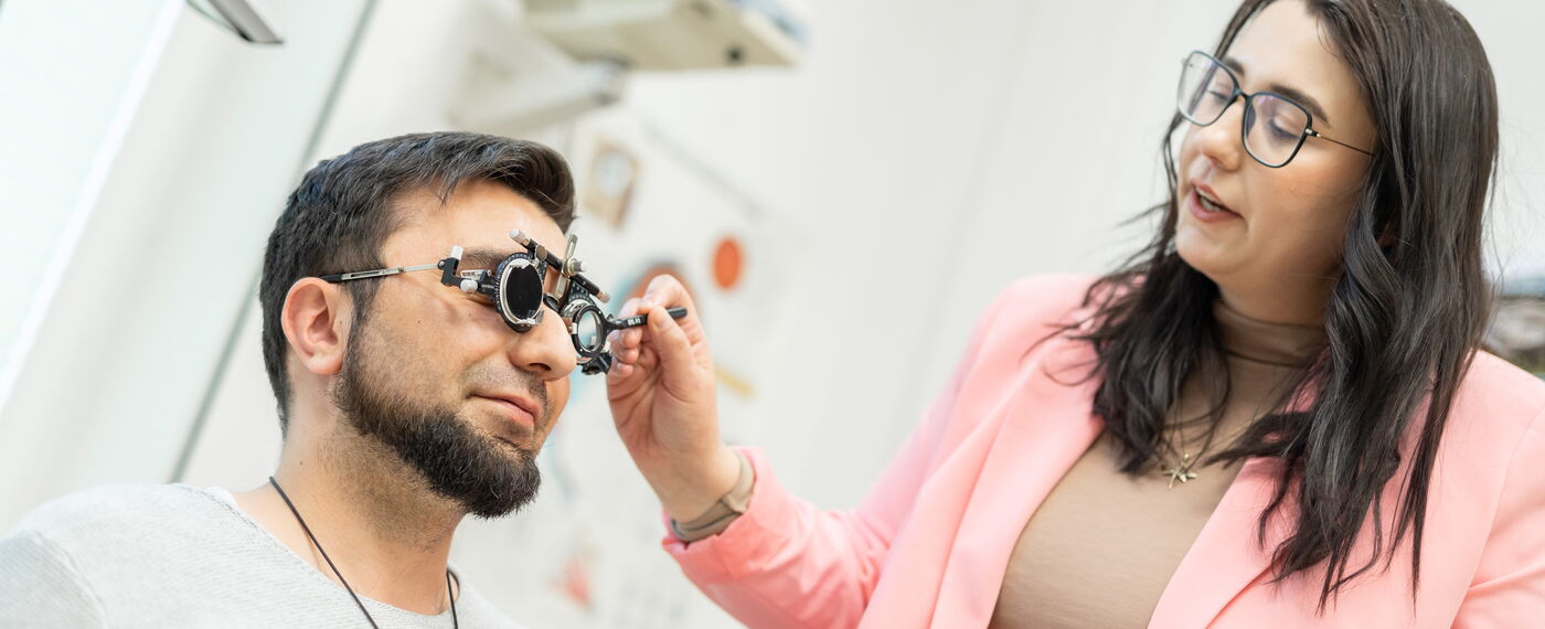Eine Low-Vision-Beraterin setzt einem Kunden bei der Refraktionsbestimmung eine Messbrille auf.