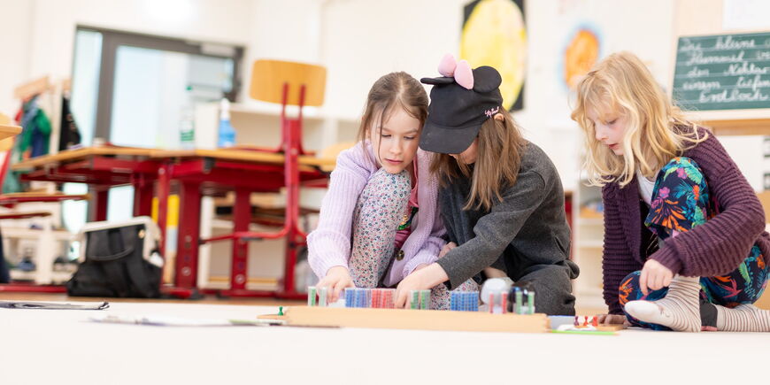 Drei Kinder arbeiten an Materialien auf dem Fußboden.