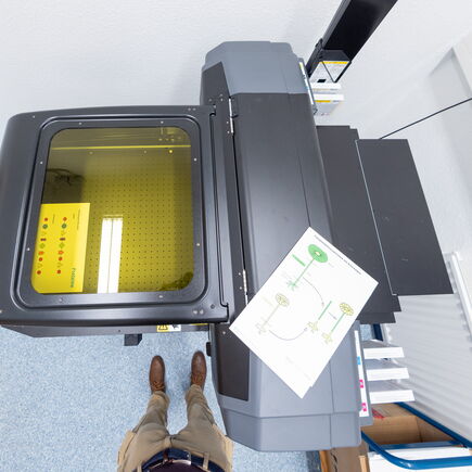 Ein UV-Drucker von oben, darauf liegt ein UV-bedrucktes Brett.