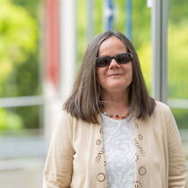 Portraitfoto Annette Stelker - sie trägt mittellanges braunes Haar, eine Sonnenbrille und ein helles Oberteil.