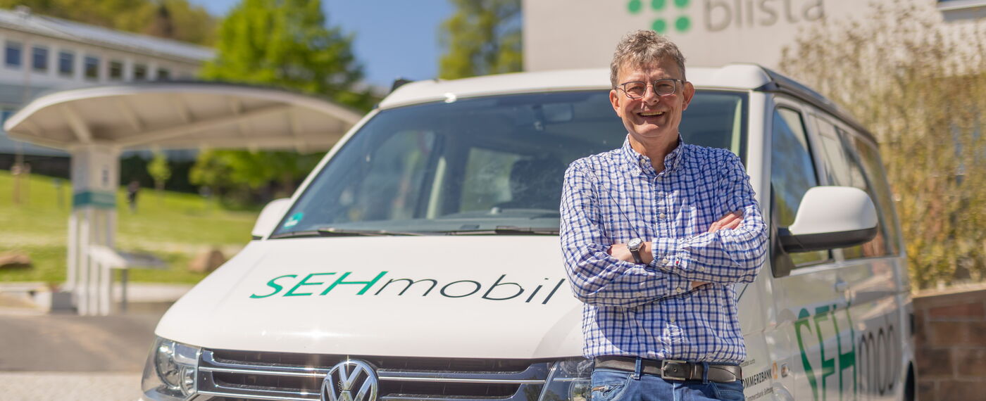 Seniorenberater Bernd Wilhelm lehnt am Sehmobil und lacht in die Kamera.
