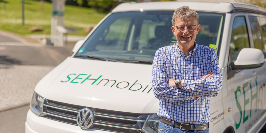 Seniorenberater Bernd Wilhelm lehnt am Sehmobil und lacht in die Kamera.