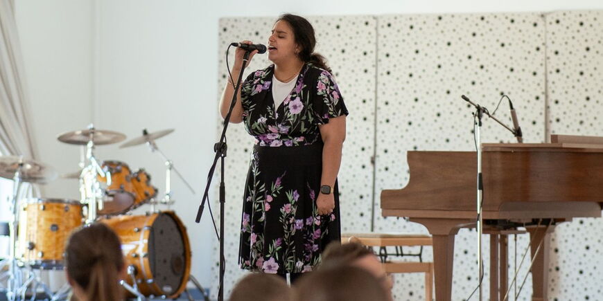Eine junge Frau steht bei der Willkommensfeier auf der Bühne und singt in ein Mikrofon.
