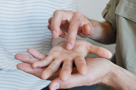 Eine Person hat die Hand einer anderen Person auf ihrer linken Hand liegen und zeichnet mit ihrer rechten Hand etwas in die Handfläche.