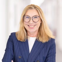 Portraitfoto Martina Borghardt - Sie trägt das blonde Haar offen, eine Brille und einen dunkelblauen Blazer mit Nadelstreifen.
