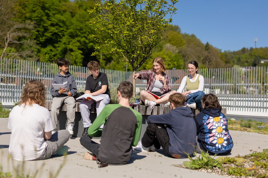 Acht Schüler*innen mit Heften auf dem Schoß sind auf der Dachterrasse in ein Gespräch vertieft.