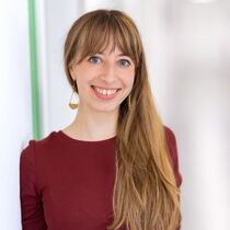 Portraitfoto Janina Pohl - Sie trägt langes, mittelblondes Haar mit Pony und ein dunkelrotes Oberteil.