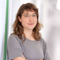 Portraitfoto Klara Bellinger - sie trägt ein graues Oberteil, eine randlose Brille und schulterlanges gelocktes Haar.