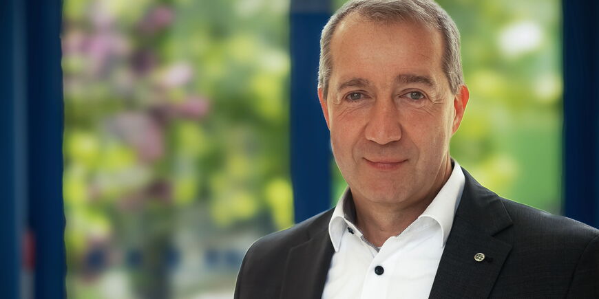Portraitfoto Patrick Temmesfeld - er hat kurzes Haar und trägt ein schwarzes Sakko auf einem weißen Hemd mit dunklen Knöpfen.