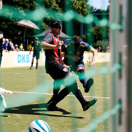 Blick durch das Tornetz beim Blindenfußball, zwei Spieler haben gerade einen Ball geschossen, den der Torwart versucht zu fangen.