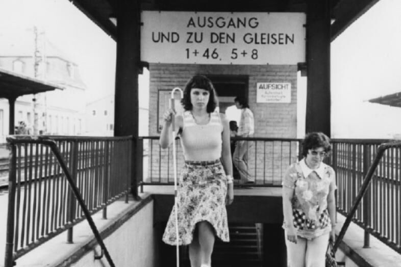Historische Fotografie einer jungen Frau, die mit Langstock in der Hand eine Treppe am Bahnhof hoch geht.