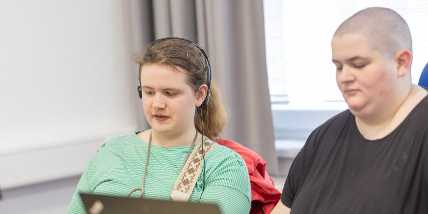 Zwei Azubis sitzen vor Laptops, eine der beiden trägt Kopfhörer