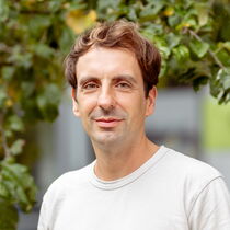 Portrait Florian Ott - Er hat braunes, kurzes Haar und trägt ein weißes T-Shirt.