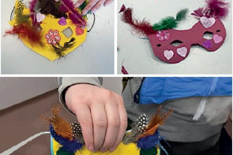 Bunte Pappmasken werden von fleißigen Händen mit Federn und Papier beklebt