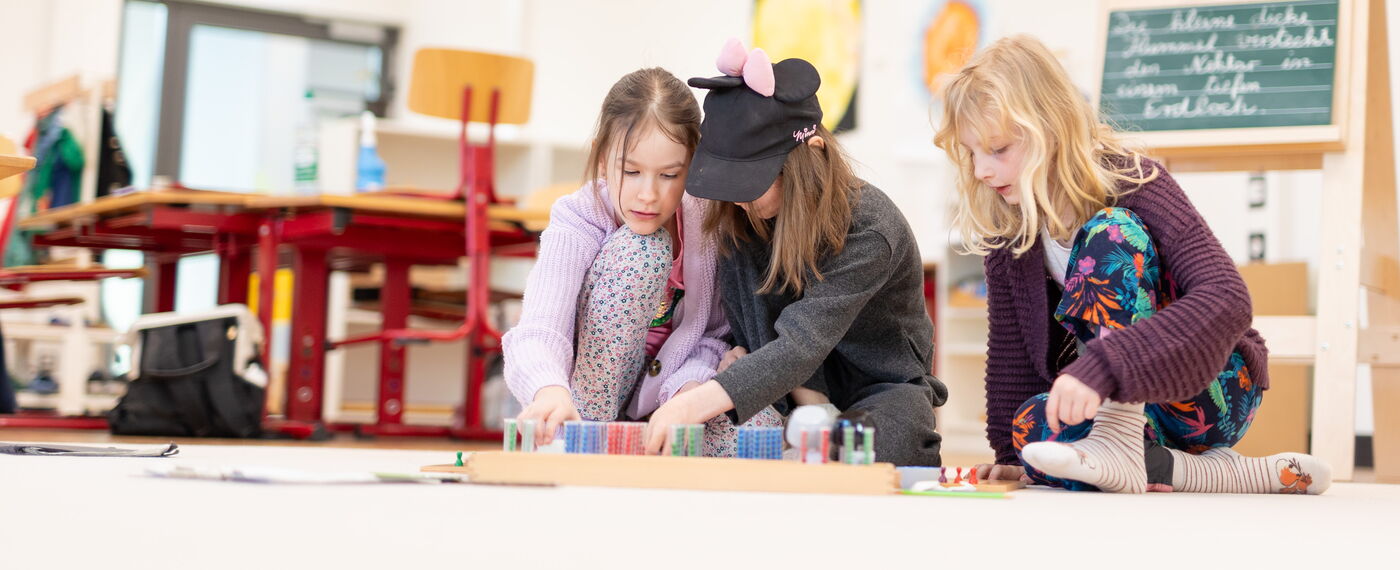 Drei Kinder arbeiten an Materialien auf dem Fußboden.