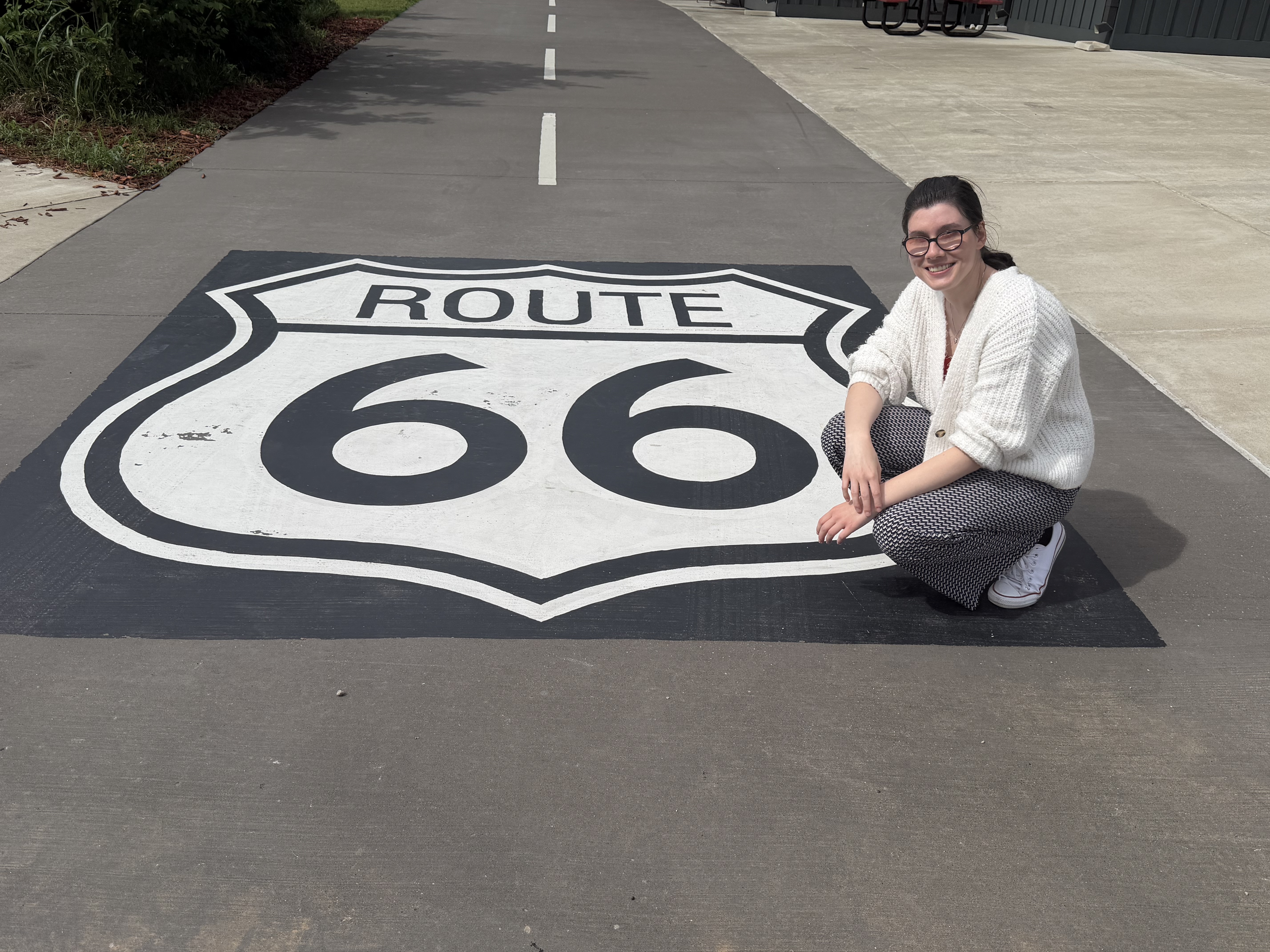 Die Autorin hockt neben einem großen, aufgemalten Schild auf einer breiten Straße, auf dem „Route 66“ steht.