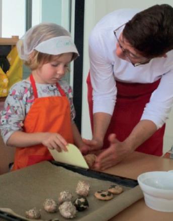 Maike Kroll bereitet zusammen mit einem konzentrierten Kinderhaus-Backtalent Gebäck auf einem Backblech zu.