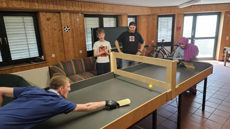 Ein Showdown-Spieler spielt mit Handschuh und Schläger auf der neuen Tischballplatte, während ihm zwei Menschen zuschauen.