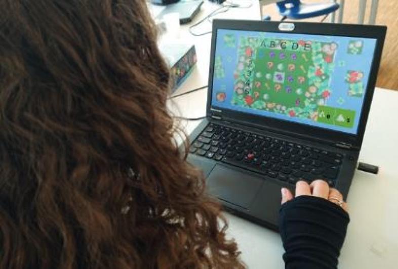 Eine Schülerin sitzt an einem Laptop, auf dessen Bildschirm ein buntes Computerspiel zu sehen ist.  