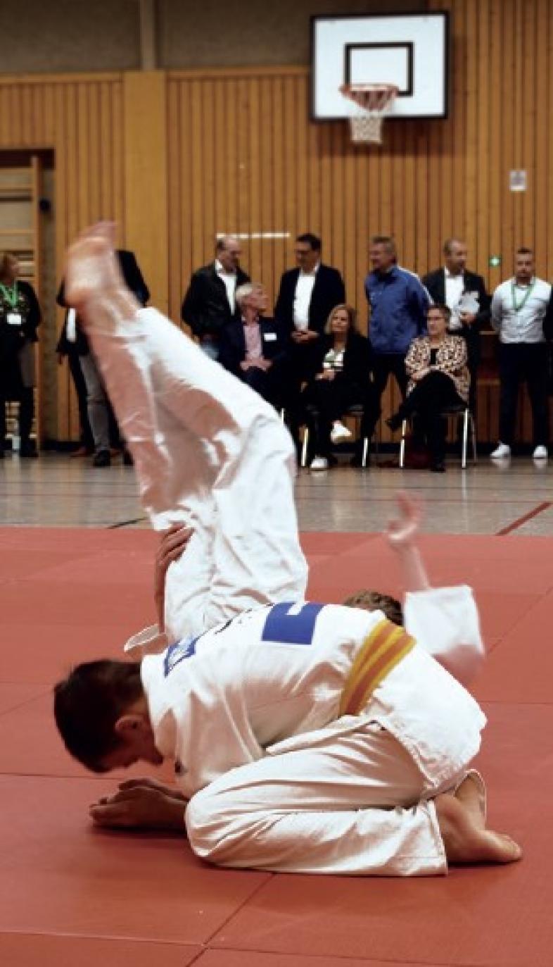 Zwei Judoka führen den Gästen auf einer roten Matte in der Sporthalle eine Übung vor.