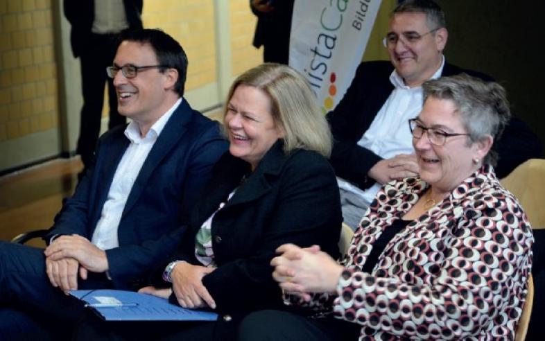 Sören Bartol, Nancy Faeser und Kirsten Dinnebier sitzen auf Stühlen im Foyer der Sporthalle und lachen fröhlich. 