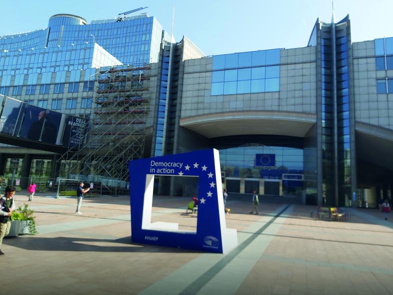 Das Bild zeigt den Eingangsbereich des Europäischen Parlaments in Brüssel. Zentral ist ein großer, blauer Rahmen mit der Aufschrift "Democracy in action" zu erkennen