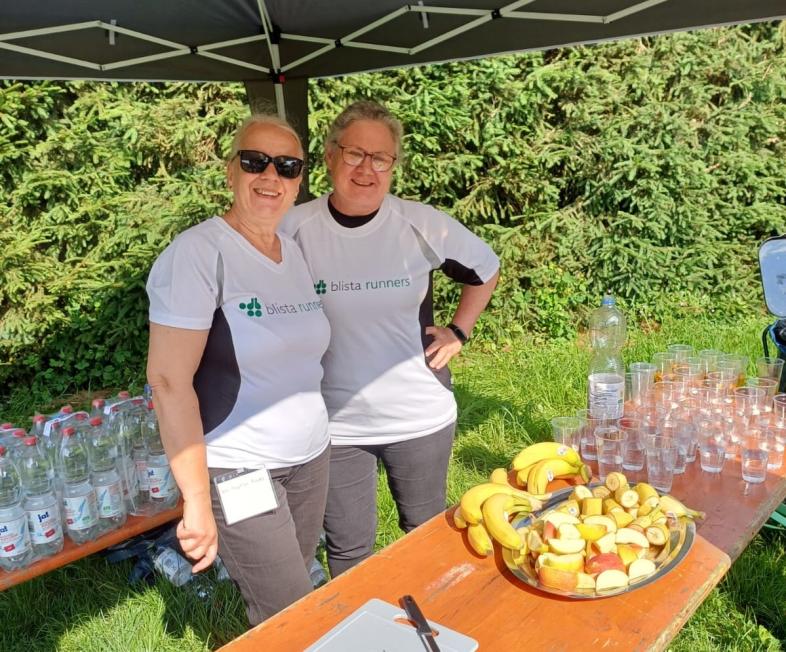 Angelika Reuter und Christel Meixner stehen im Schatten eines Pavillons und lächeln in die Kamera. Vor ihnen Obst und Wassergläser