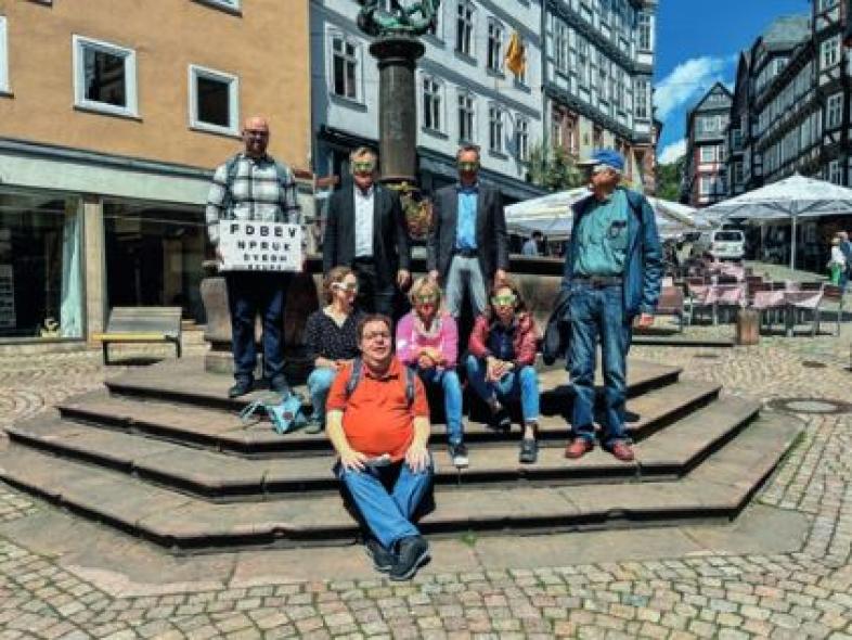 Ein Gruppenbild der 8 Teilnehmenden des Oberstadtspaziergangs auf dem Marburger Marktplatz, darunter auch Spies und Temmesfeld. Einige tragen Simulationsbrillen in grün, um einen Sehrest von unter 10% zu simulieren. 